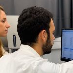 Two researchers in lab coats reviewing data on a computer screen in a cancer research lab in Israel